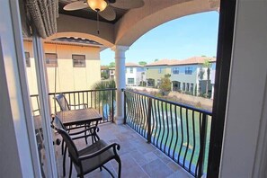 A balcony with a table and chairs, a view of neighboring houses, and a clear sky.