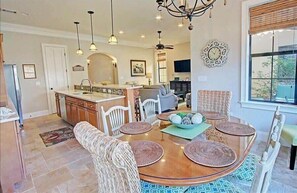 A spacious kitchen with a central island, white chairs, and a dining table with woven placemats.