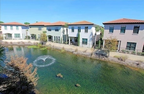 A residential area with a clear water feature, houses with red-tiled roofs, and a paved walkway.