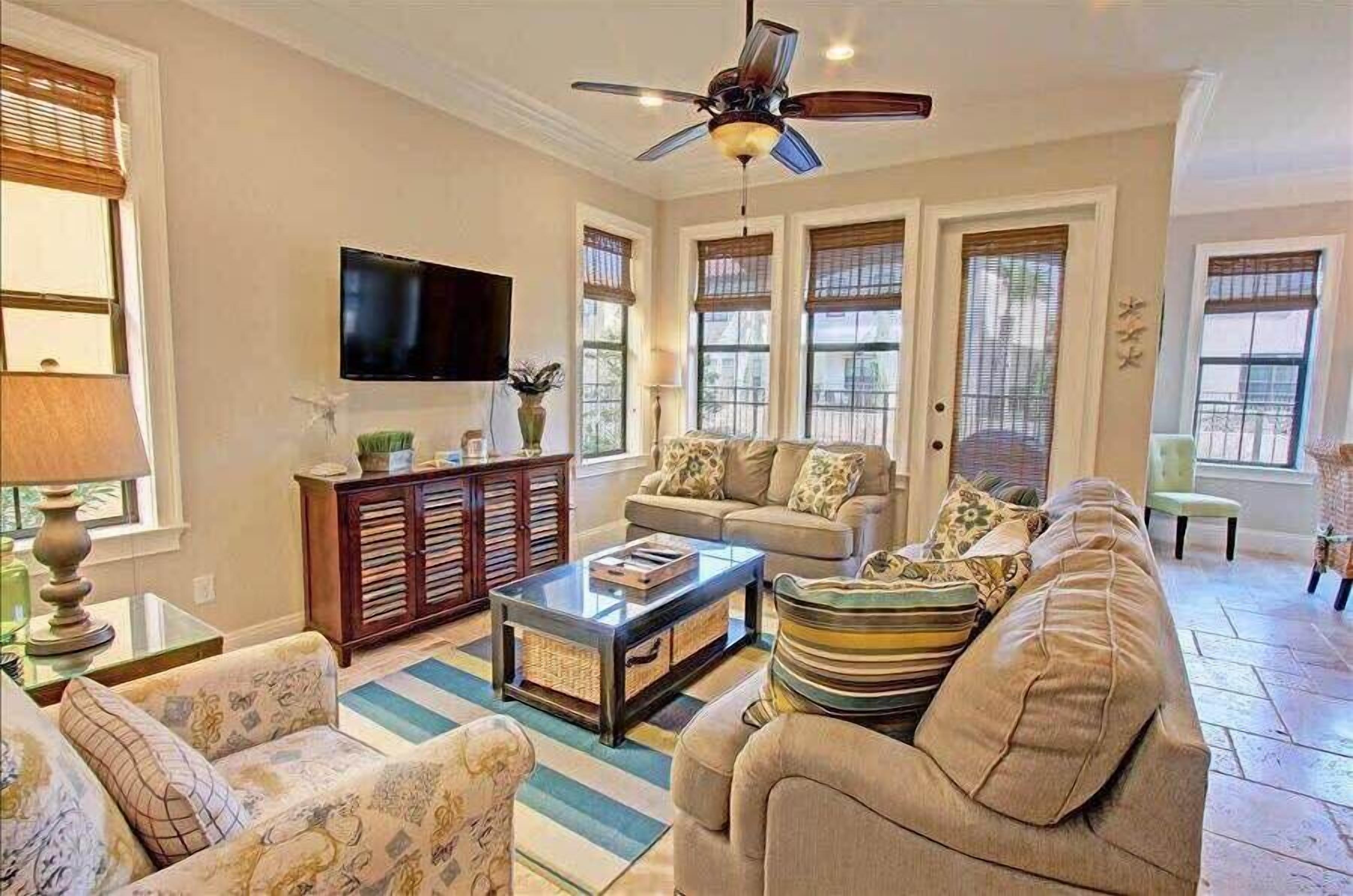 A spacious living room with a ceiling fan, a flat-screen TV, a sofa set, and a coffee table.