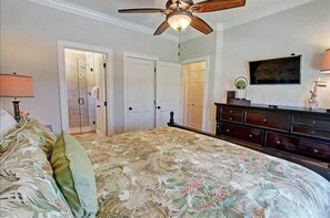 A bedroom with a bed, a dresser, a ceiling fan, and a door leading to another room.