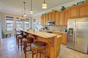 A kitchen with wooden cabinets, a stainless steel refrigerator, a large island with stools, and pendant lighting. - Luxury at 2,000+ SqFt! Baytowne and Pool! Golf Cart! Pond View! - Poppy's Place at Villa Lago Sandestin® (Miramar Beach)