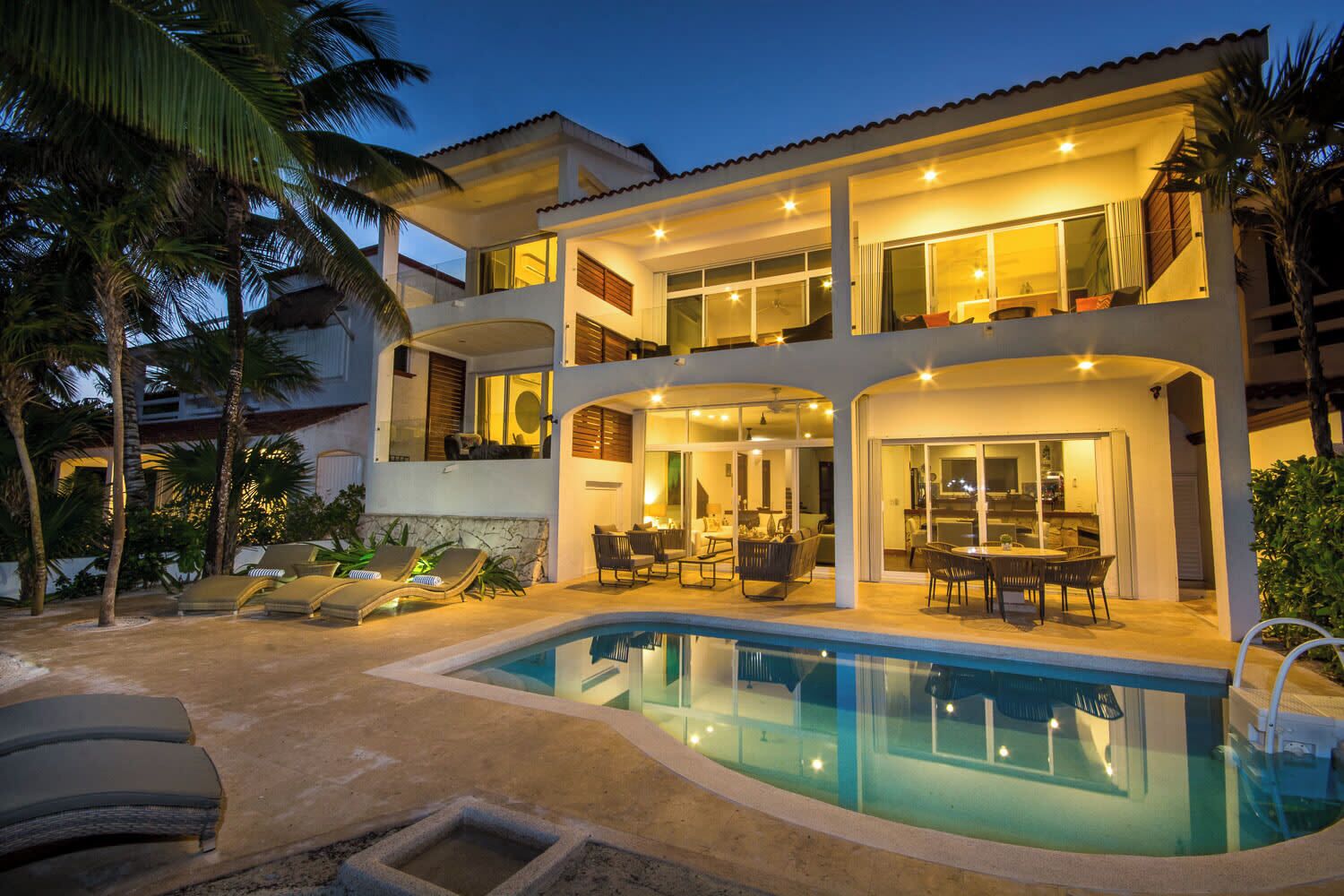 Ein zweistöckiges Haus mit Swimmingpool, Sitzgelegenheiten im Freien und einer überdachten Terrasse.