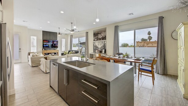 A modern kitchen with a central island, a dining area with a view, and a living space with a TV.