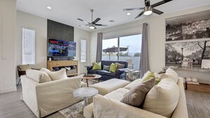 A modern living room with a large flat-screen TV, two sofas, a coffee table, and a ceiling fan.