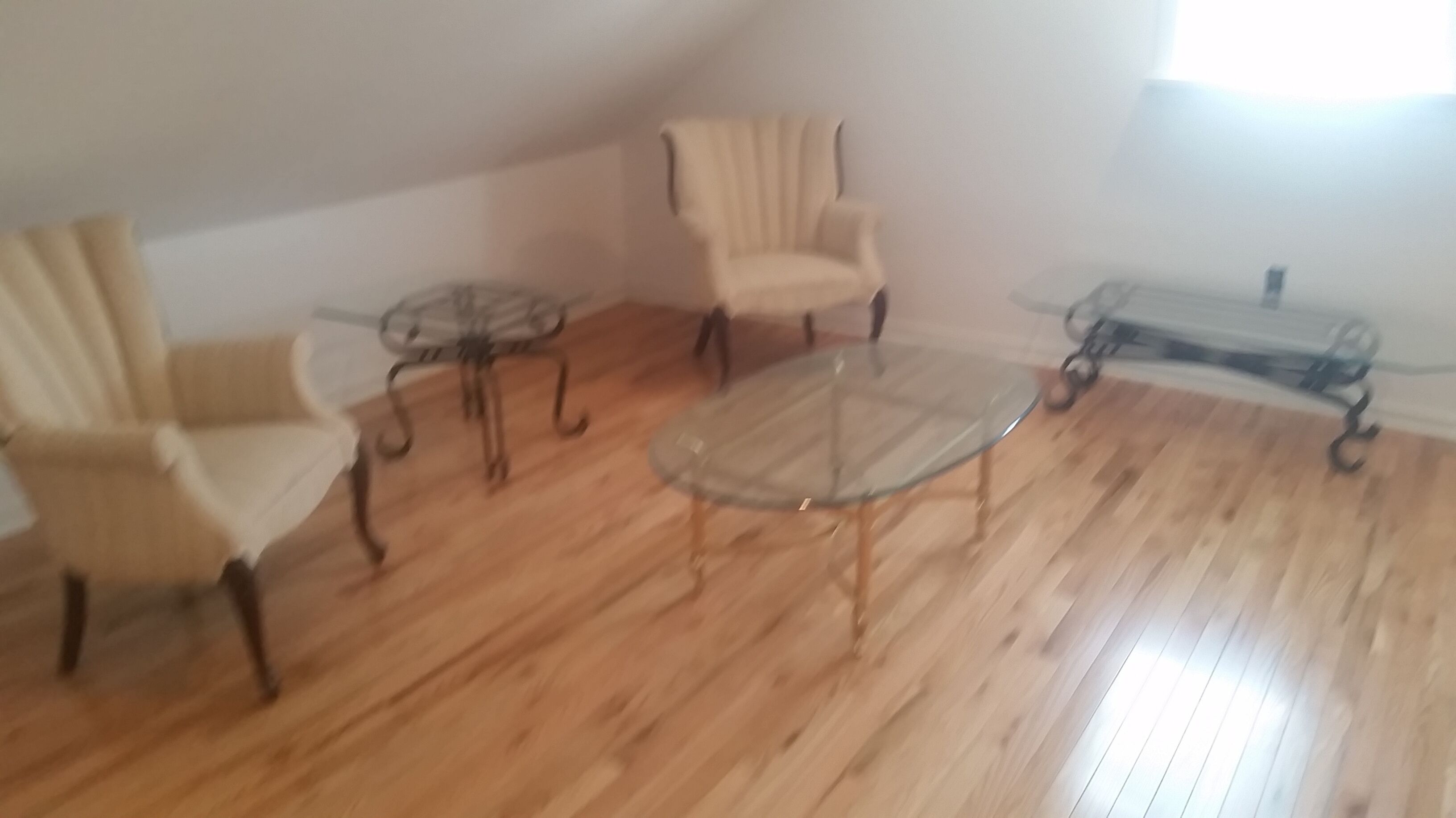 Une pièce avec un plancher en bois, une table basse en verre et deux fauteuils.