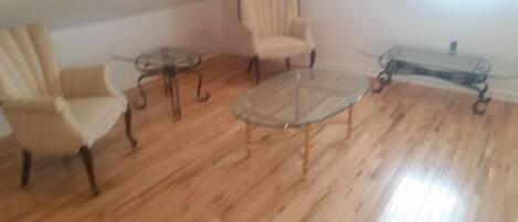 Une pièce avec un plancher en bois, une table basse en verre et deux fauteuils.