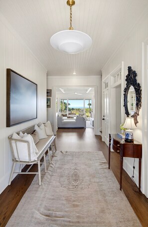 A hallway with a white bench, a large mirror, and a view into a living area with a sofa and a table. - Discounts! 🌊Oceanfront! 2204 Palm~ beautifully decorated, elevator, pool, hot tub (Isle Of Palms)