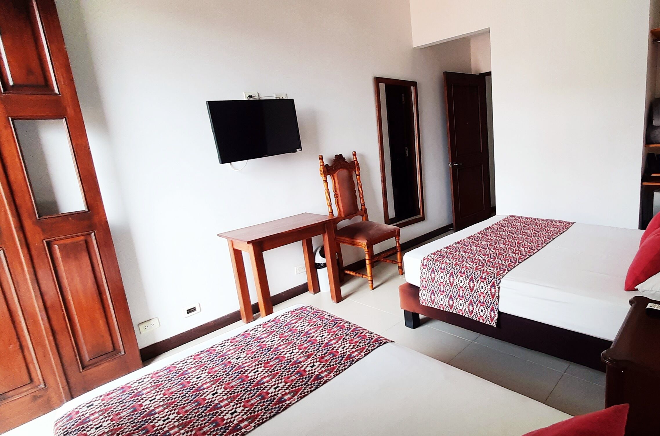 Una habitación de hotel con dos camas, un escritorio de madera, una silla, un televisor y un espejo.