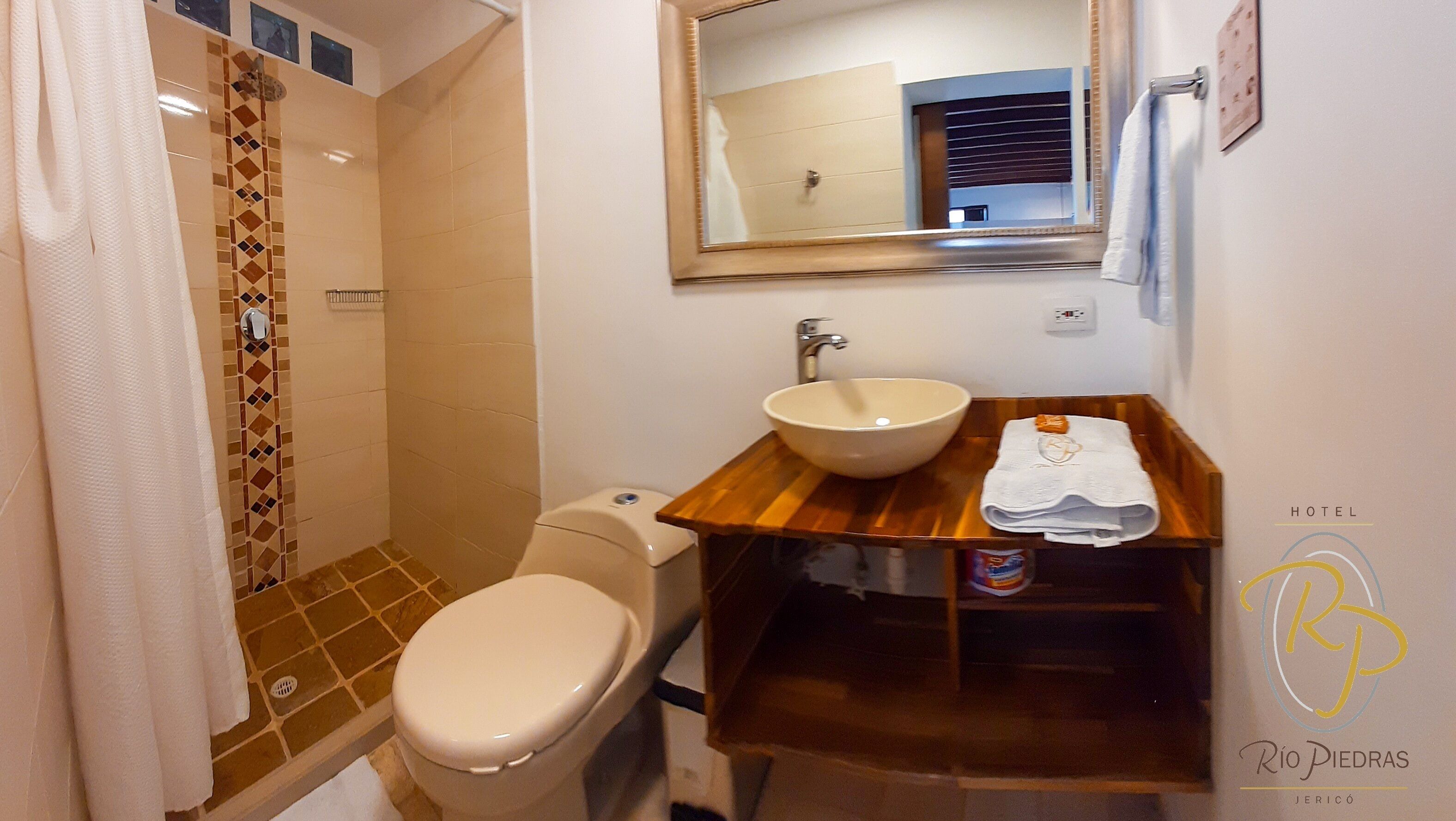 A bathroom with a toilet, a sink with a mirror above it, and a shower area with a tiled wall.