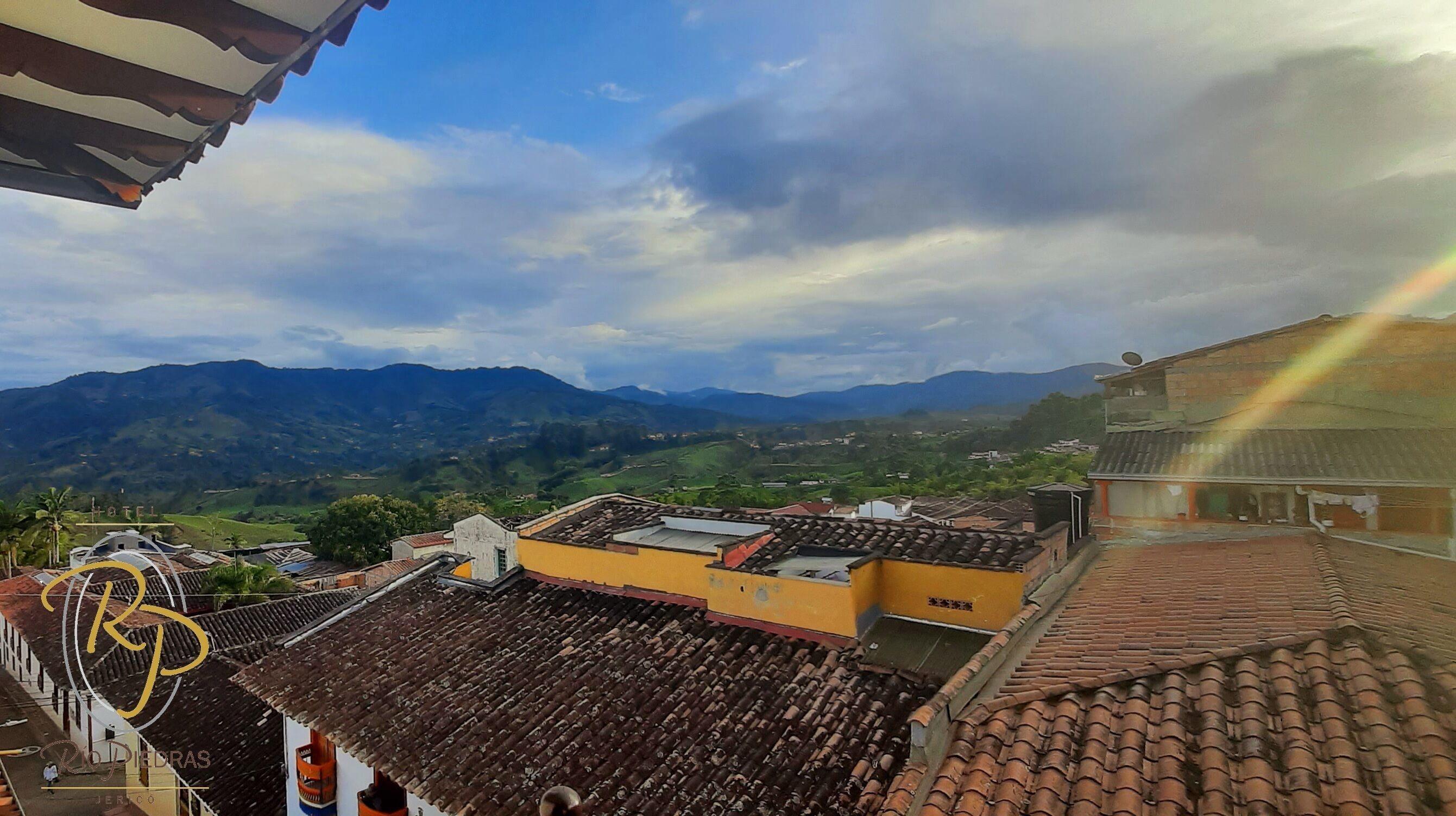 A view of a town with terracotta-roofed buildings, a mountain range in the background, and a clear sky.