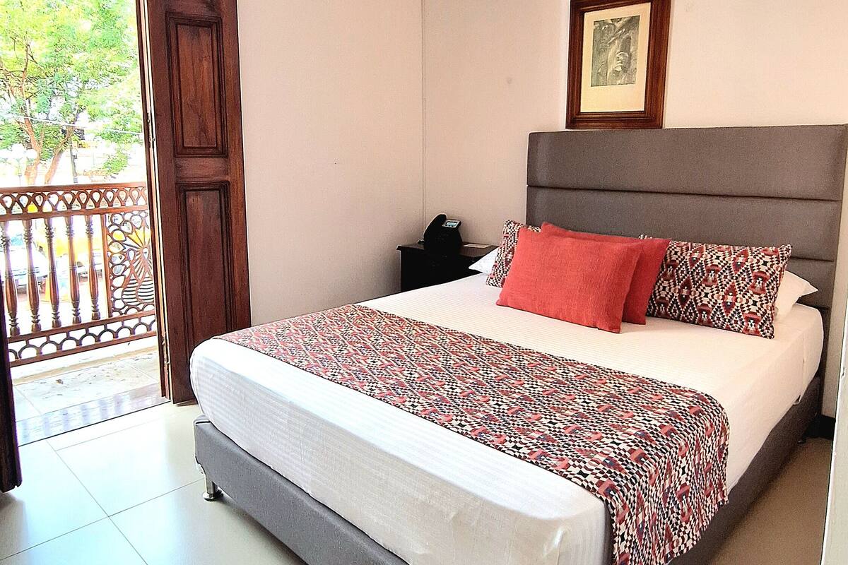 A hotel room with a bed, a nightstand, a framed picture on the wall, and a balcony door.