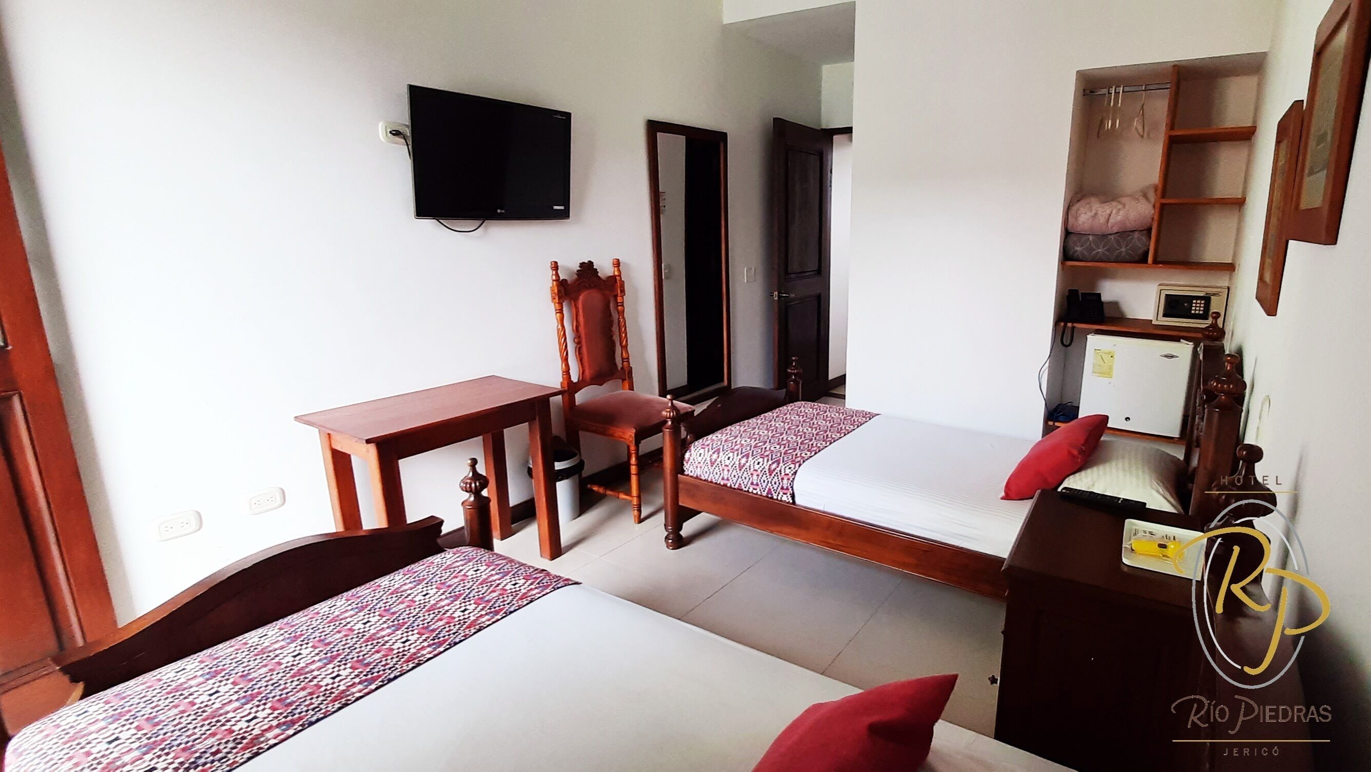 A hotel room with two beds, a desk, a chair, a television, and a wardrobe.