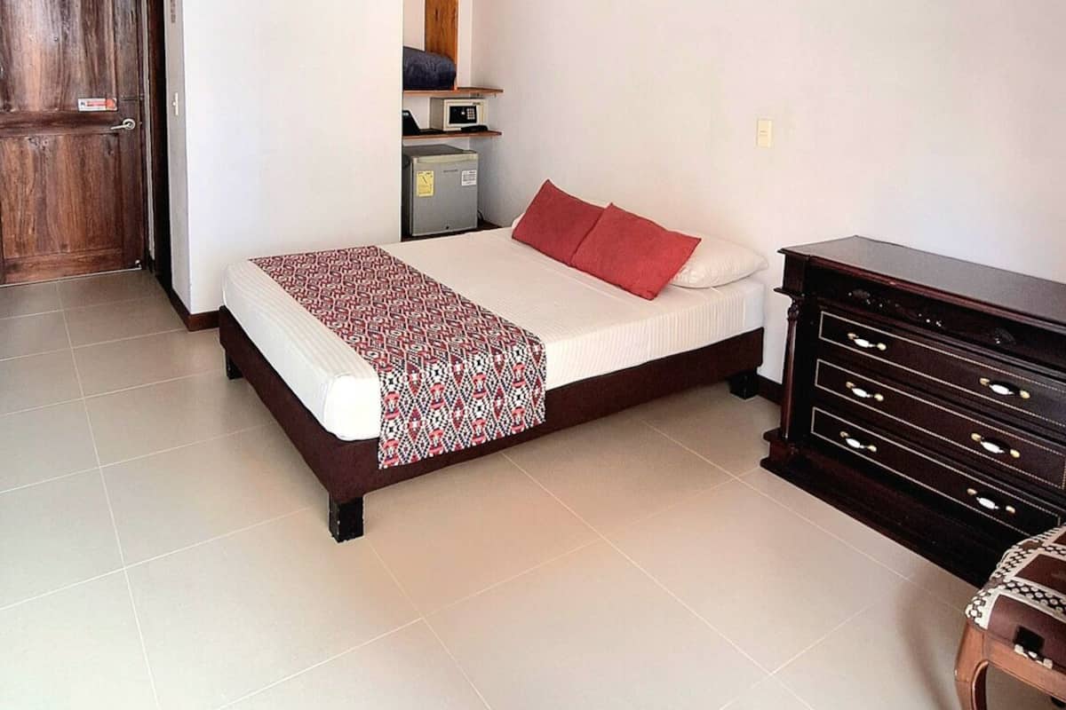 A hotel room with a bed, a dresser, a microwave, and a small cabinet.