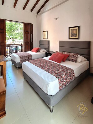 A hotel room with two beds, a balcony, and a view of greenery outside. - Hotel Rio Piedras (Jericó)