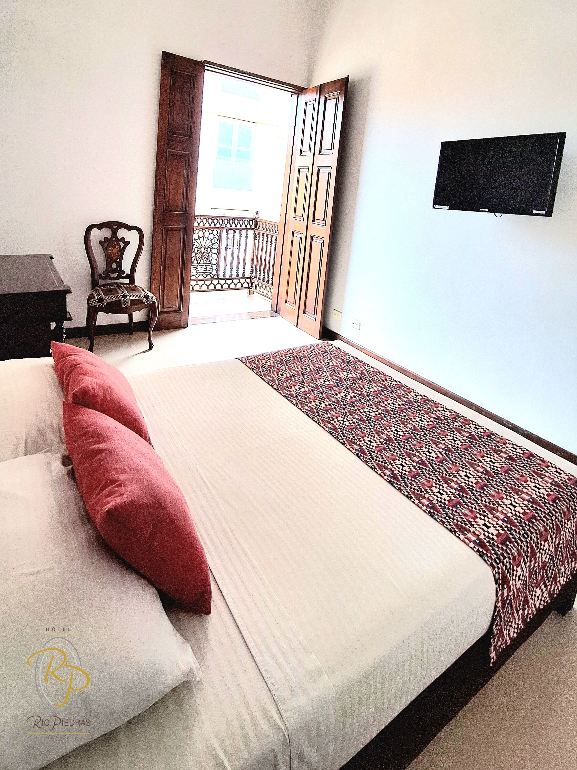 Una camera d'albergo con un letto, cuscini, una TV, una sedia e un balcone.