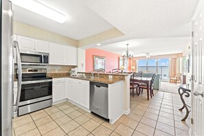 A modern kitchen with white cabinets, stainless steel appliances, a granite countertop, and a dining area with a view.