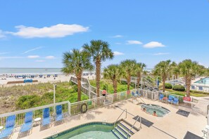 A pool area with a view of the beach, palm trees, and a staircase leading to a deck.