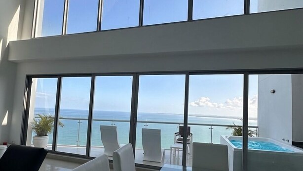Een moderne eetruimte met een glazen tafel en witte stoelen, met uitzicht op een zwembad en de oceaan.