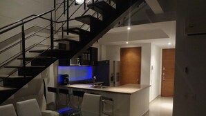 Een moderne keuken met een centraal eiland, een eethoek met glazen tafels, en een trap naar een hoger gelegen verdieping.