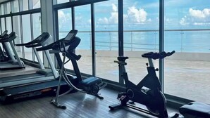 Een sportschool met loopbanden en hometrainers, grote ramen en uitzicht op zee.