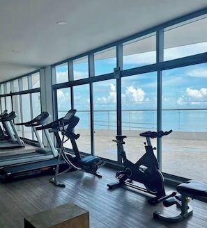 A gym with treadmills and stationary bikes, large windows, and a view of the sea.
