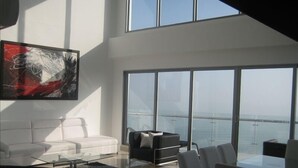 Een moderne woonkamer met een groot raam, een witte bank, een zwarte bank en een glazen salontafel.