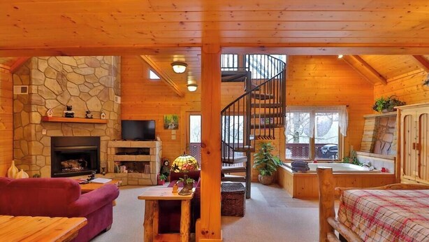 A cozy cabin interior with a stone fireplace, a wooden staircase, and a comfortable seating area.