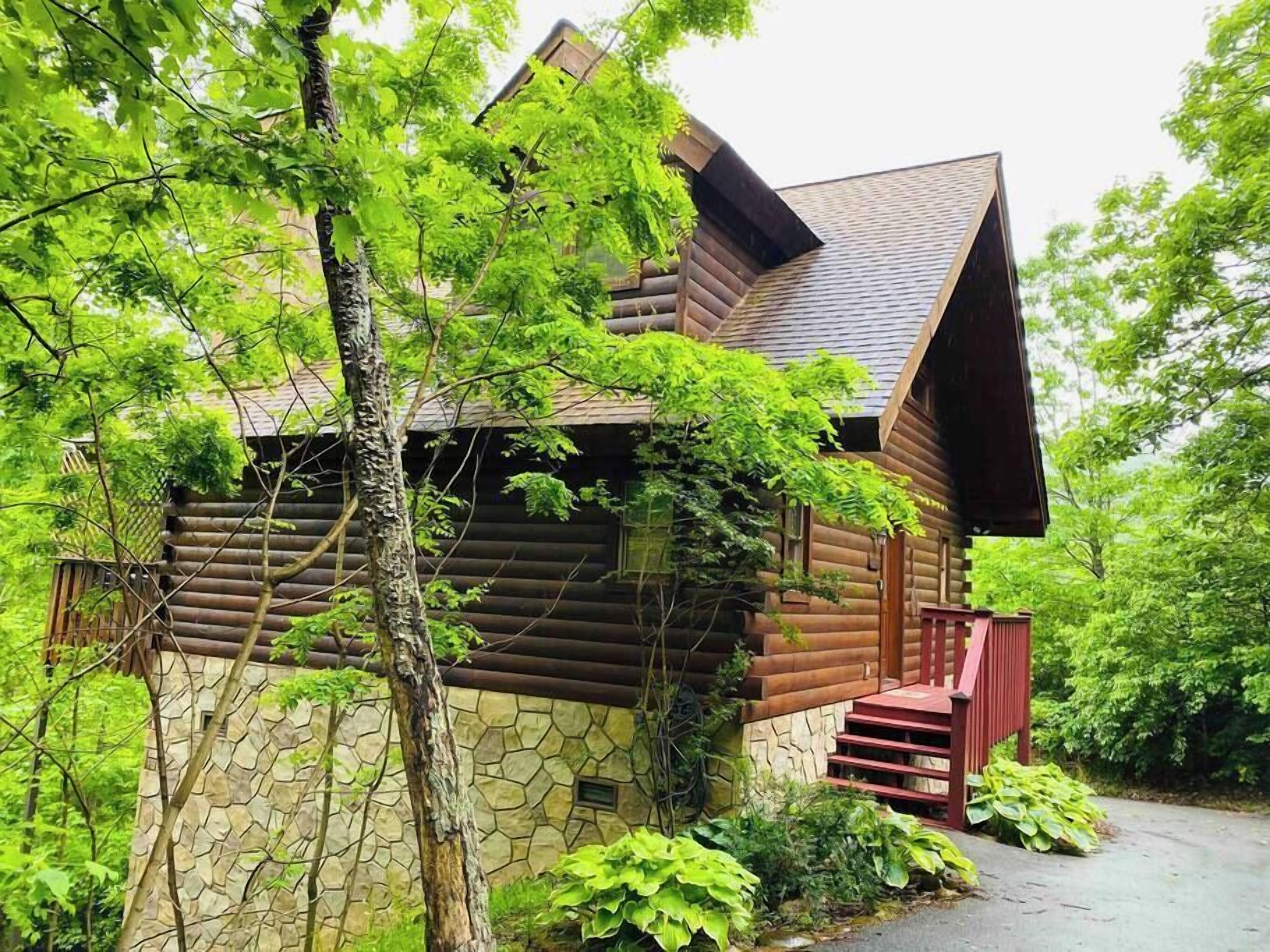 Une cabane en rondins, avec des fondations en pierre, un toit à forte pente et un escalier rouge menant à l’entrée.