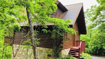 Une cabane en rondins, avec des fondations en pierre, un toit à forte pente et un escalier rouge menant à l’entrée.