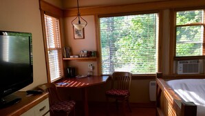 Una habitación pequeña con escritorio de madera, dos sillas, televisor, radiador y ventana con persianas.