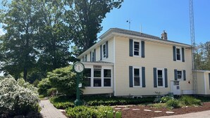 A two-story building with a clock, a sign indicating an office, and a garden area with plants and a pathway. - Maple Lane Empire (Empire)