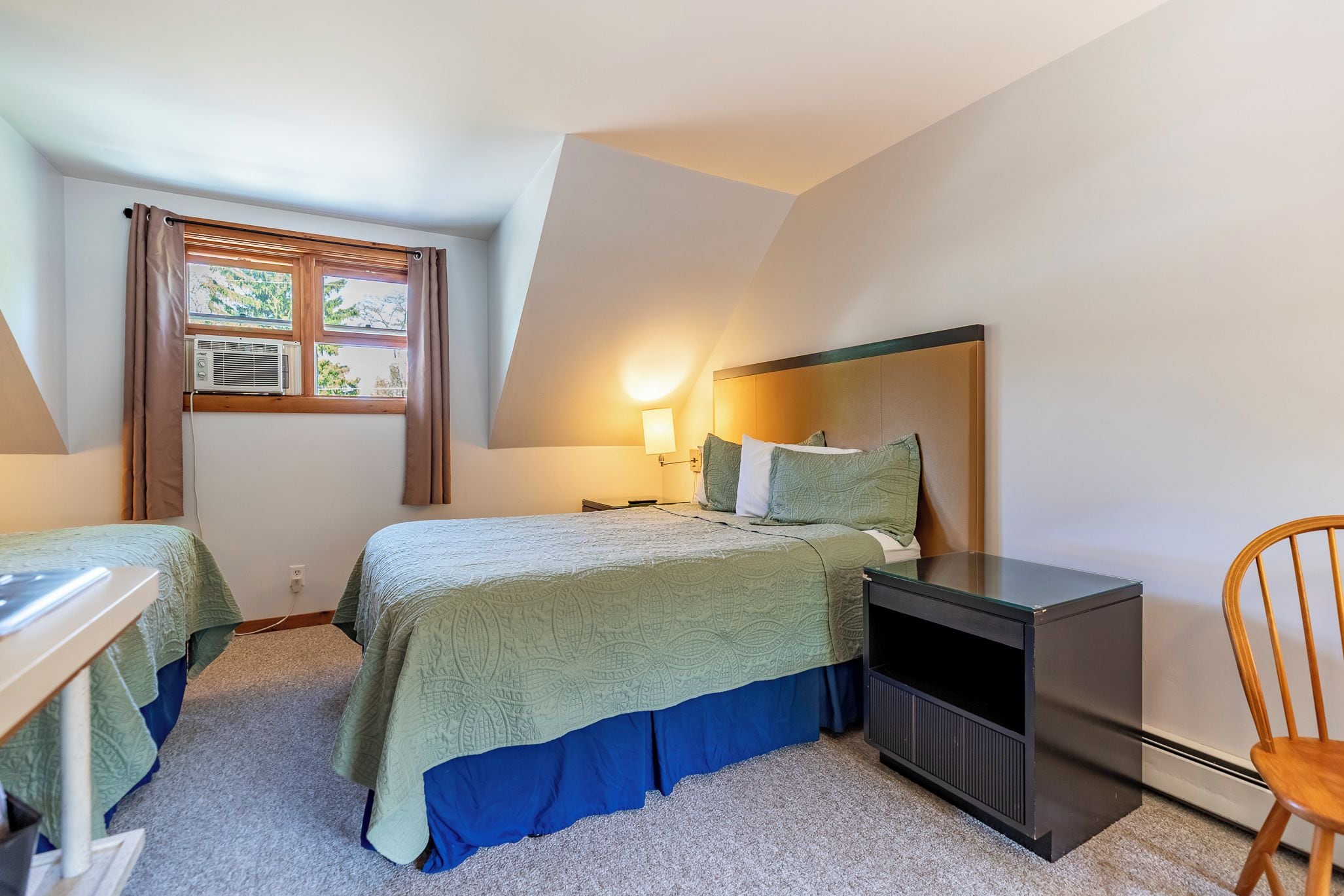 Ein Schlafzimmer mit Bett, Nachttisch, Lampe und einem Sessel.