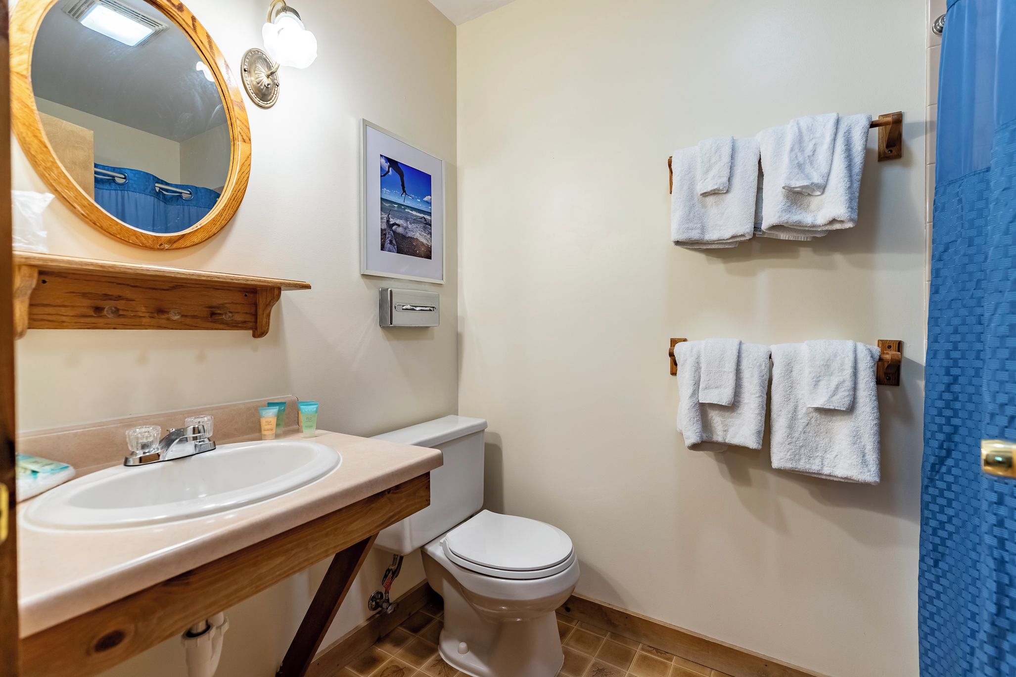 A bathroom with a wooden vanity, a white sink, a toilet, and two towel racks with white towels.