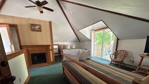 A cozy attic bedroom with a sloped ceiling, a wooden bed, a fireplace, and a large window offering a view of the outdoors. - Maple Lane Empire (Empire)