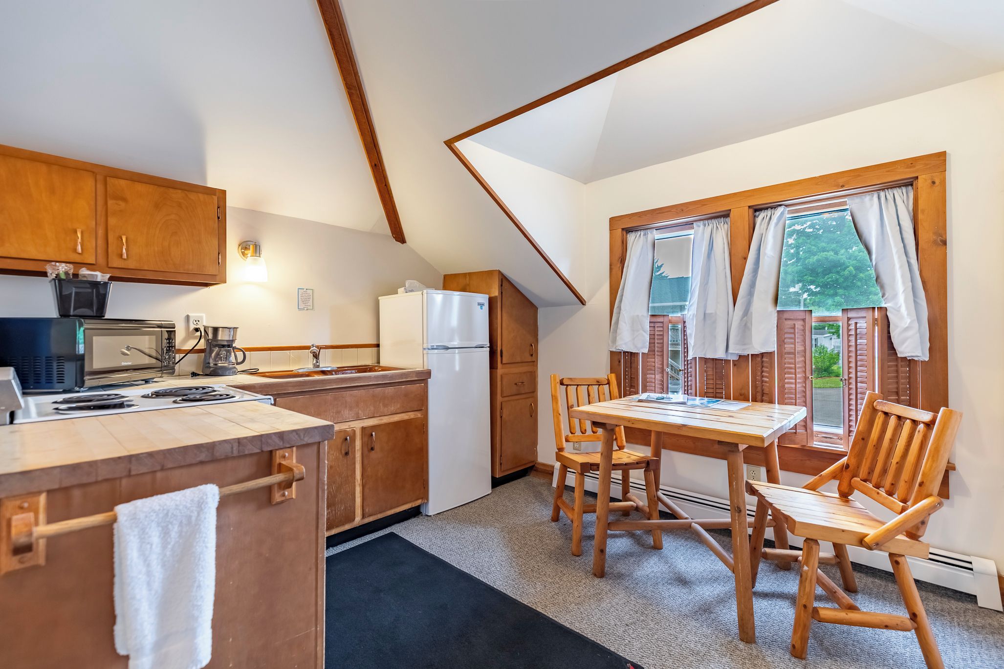 A compact kitchen with wooden cabinets, a refrigerator, and a dining area with a table and chairs.