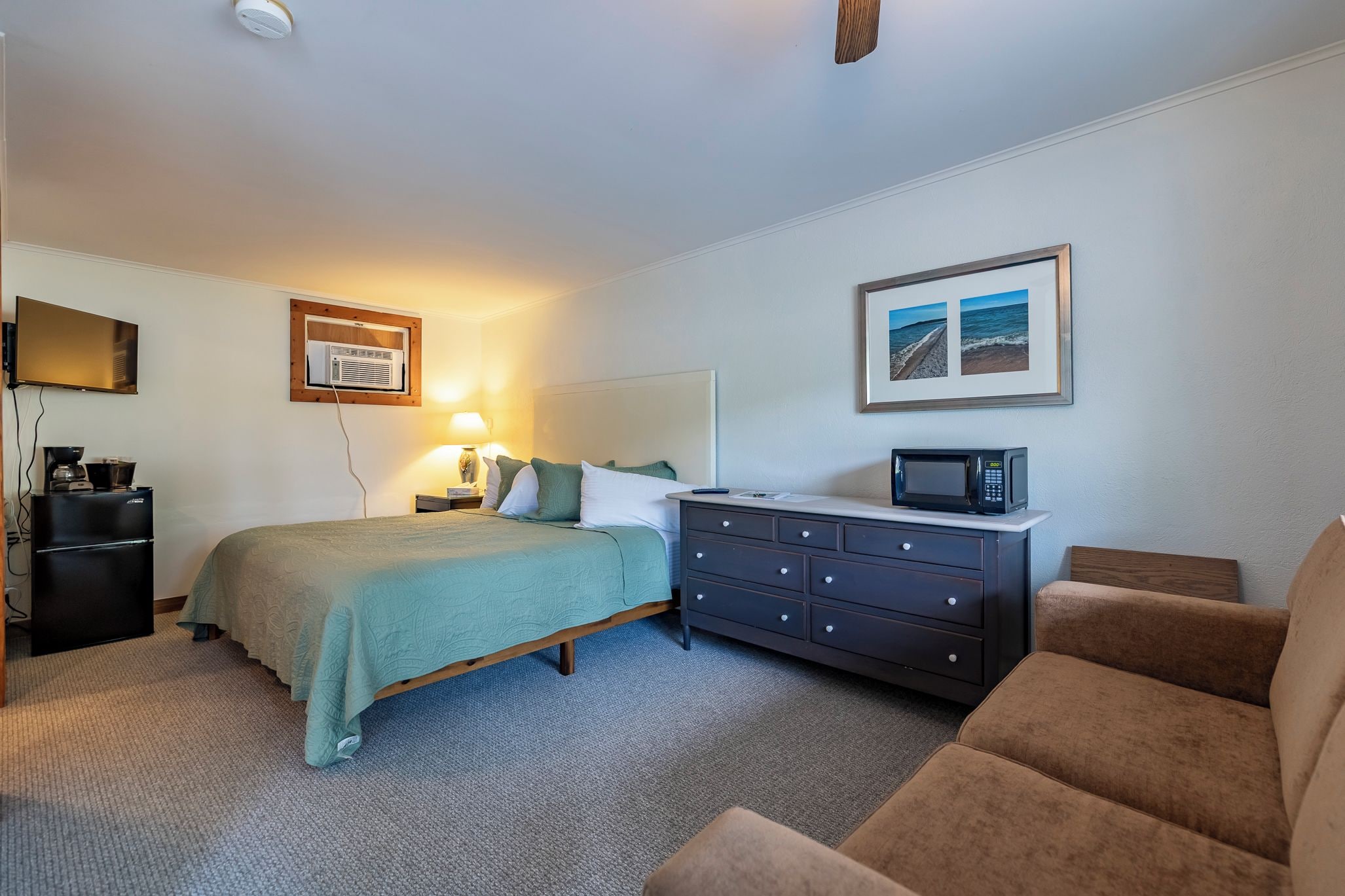 A hotel room with a bed, a dresser, a microwave, a television, and a framed picture on the wall.