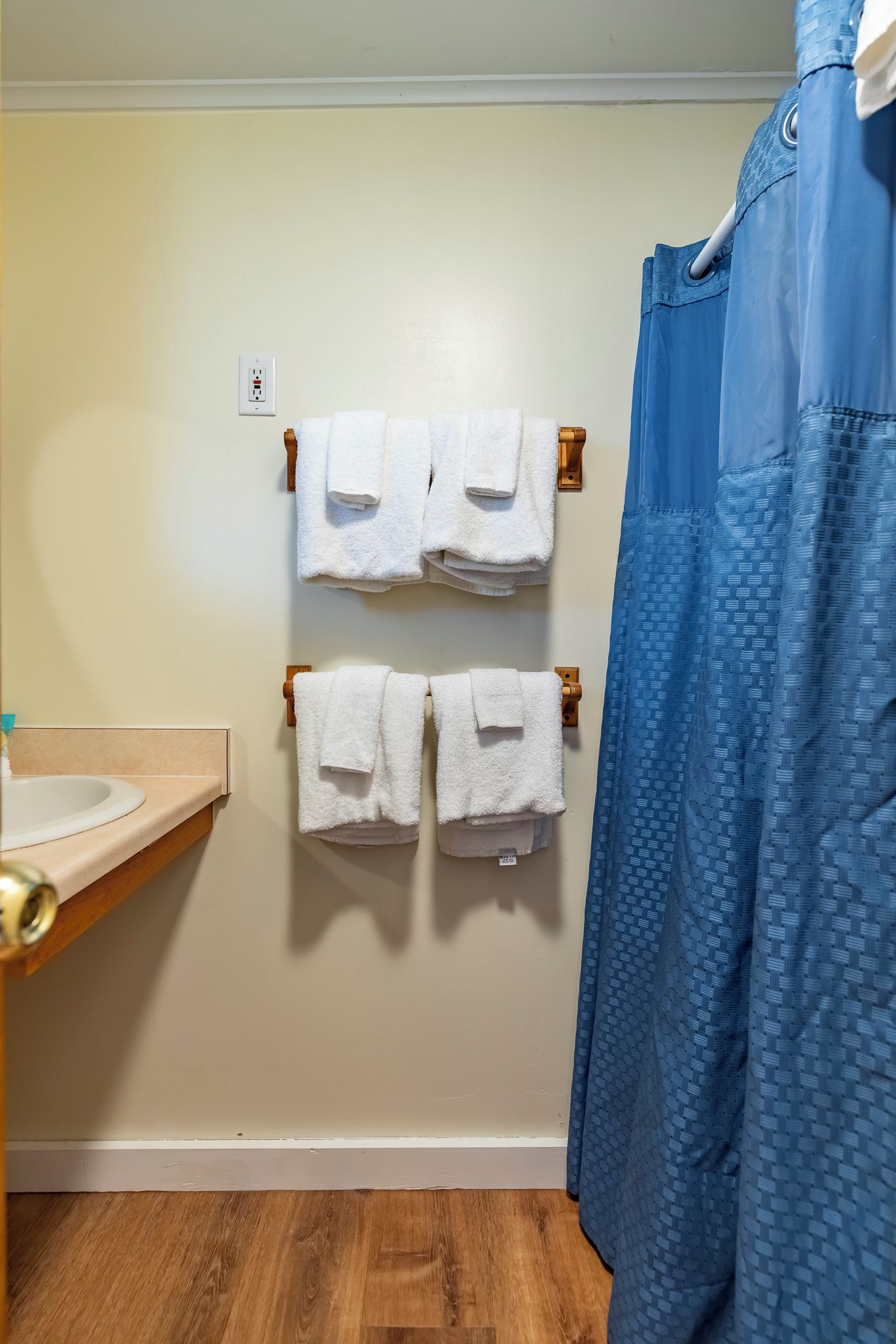 A bathroom with two towel racks holding white towels, a blue shower curtain, and a wooden floor.