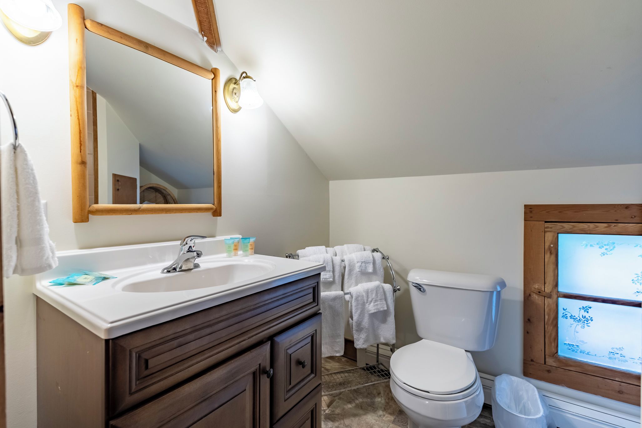 A bathroom with a white sink, dark wooden vanity, a toilet, and a mirror.