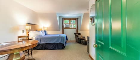 Une chambre à coucher avec un lit, des tables de chevet, un bureau, une chaise, une porte verte et une fenêtre.
