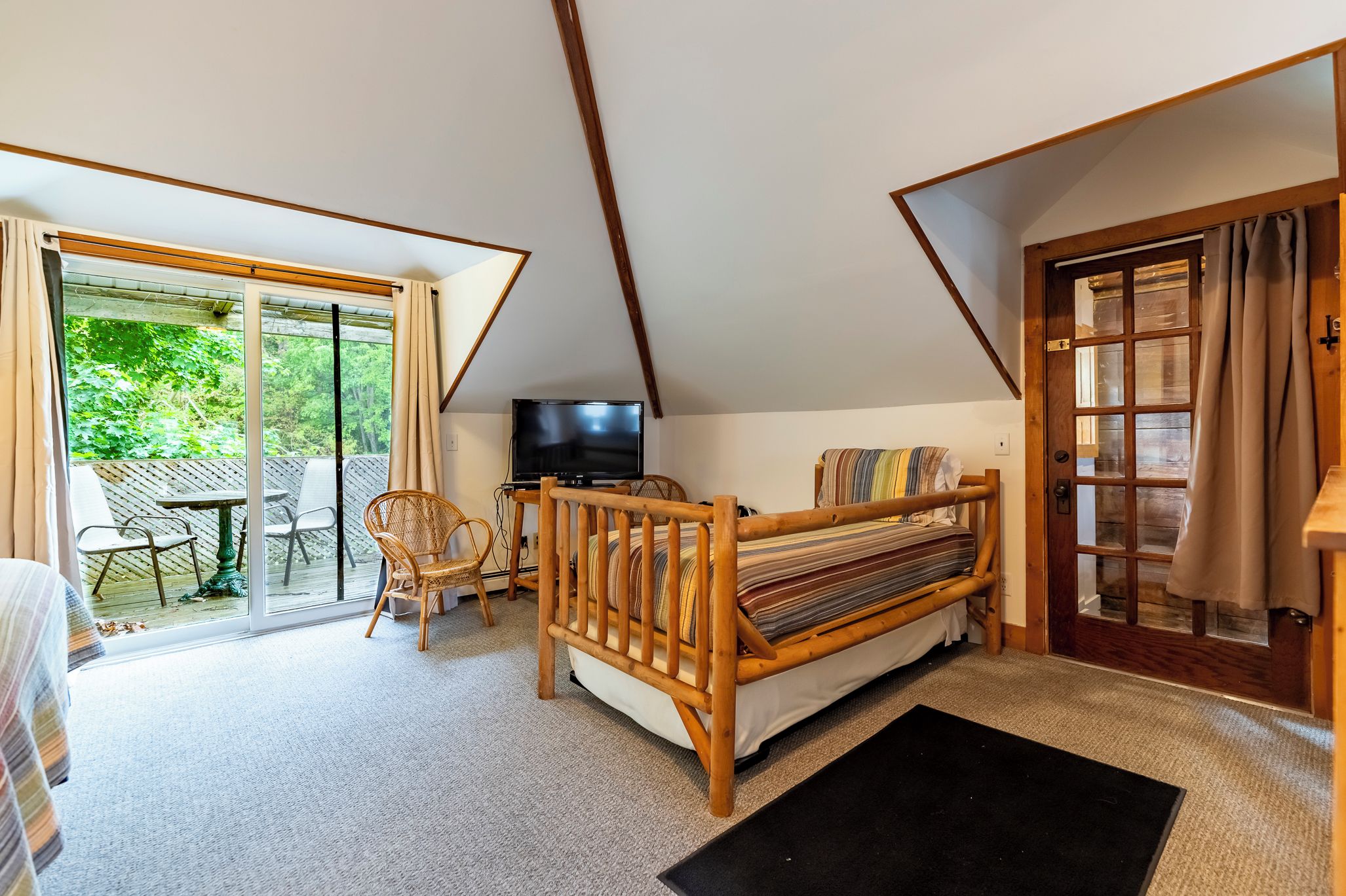 A bedroom with a bed, a television, a chair, and a view of the outdoors.