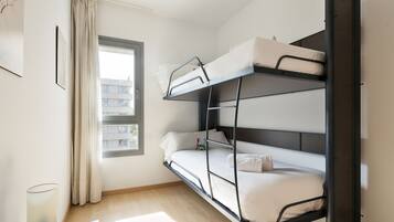 Habitació amb un llit superposat, una finestra, cortines i una làmpada.