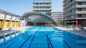 Ein Schwimmbecken mit deutlichen Bahnen, umgeben von modernen Gebäuden mit mehreren Etagen und Balkonen.