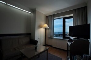 A hotel room with a sofa, a table, a lamp, a TV, and a window with curtains. - Kadikoy Rihtim Hotel (Istanbul)