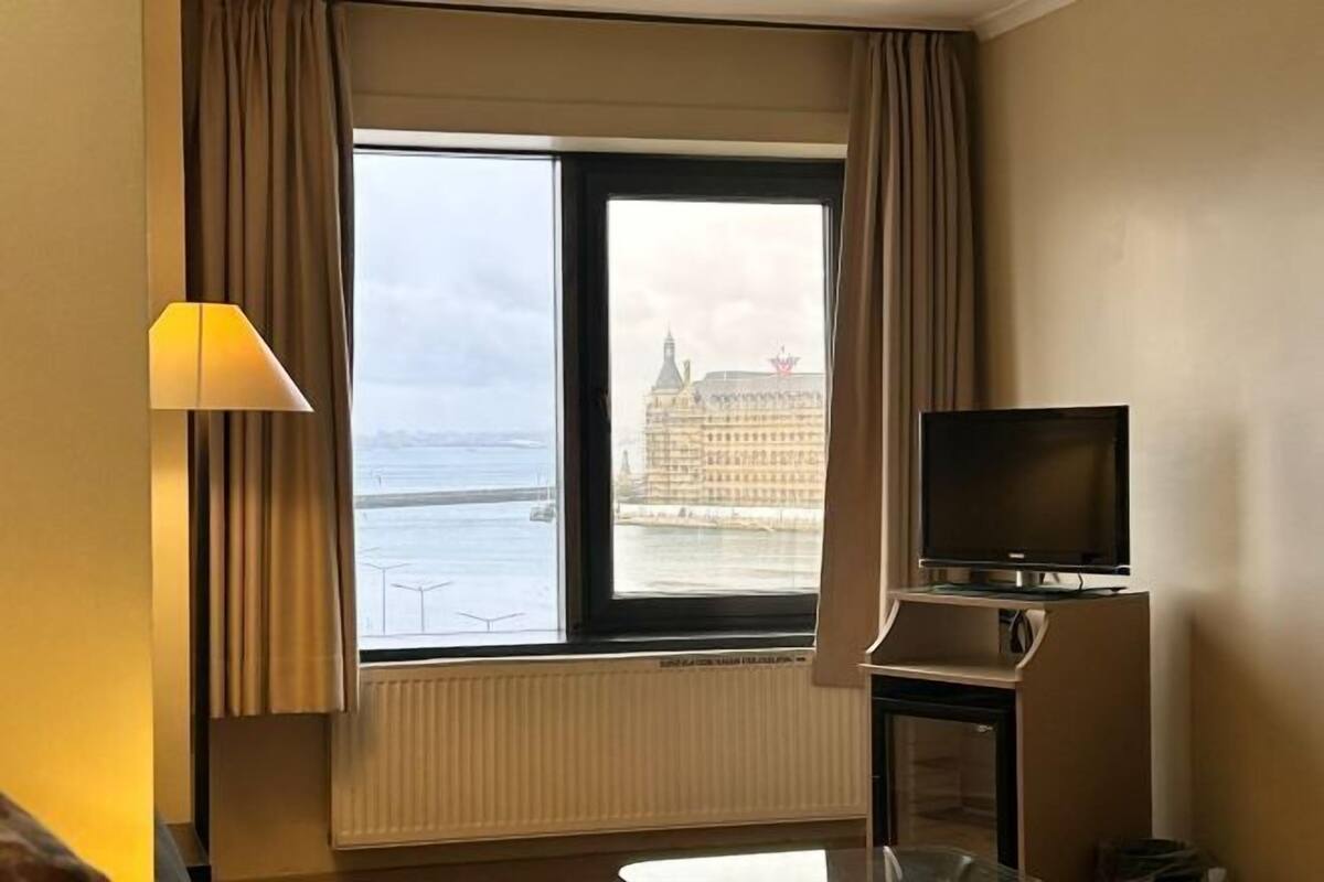 A hotel room with a large window, a television, and a lamp.