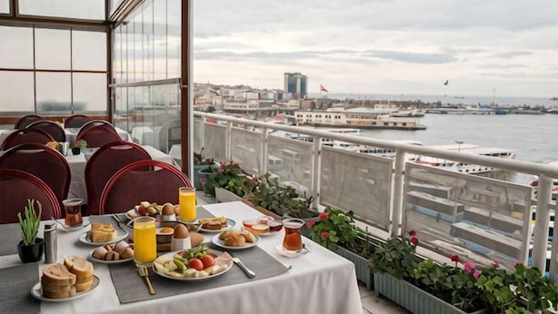 A dining area with a table set for two, overlooking a waterfront with a cityscape in the background. - Kadikoy Rihtim Hotel (Istanbul)