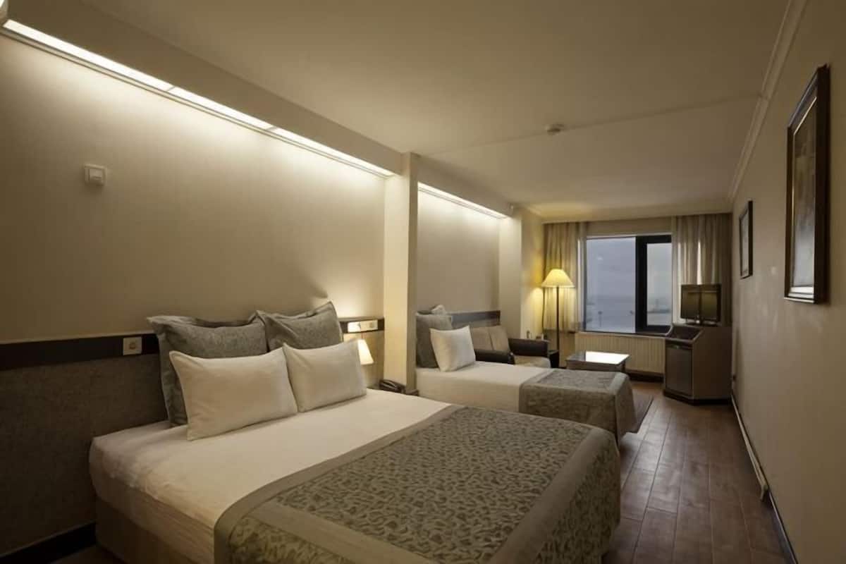 A hotel room with two beds, a large window, a desk, and a mirror.
