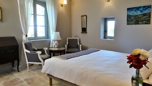 A bedroom with a bed, two chairs, a desk, a lamp, a painting, and a vase with flowers. - Chambre d'hôtes Château MontPlaisir (Valreas)