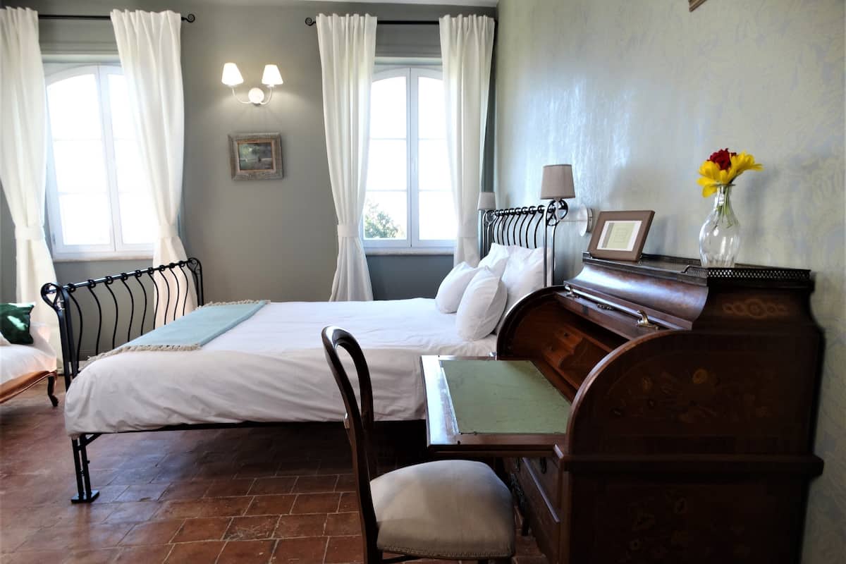 Ein Schlafzimmer mit einem Bett, einem Klavier, einem Sessel und einem Fenster mit Vorhängen.