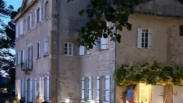 A group of people dining at an outdoor table by a pool, with a large building in the background. - Chambre d'hôtes Château MontPlaisir (Valreas)